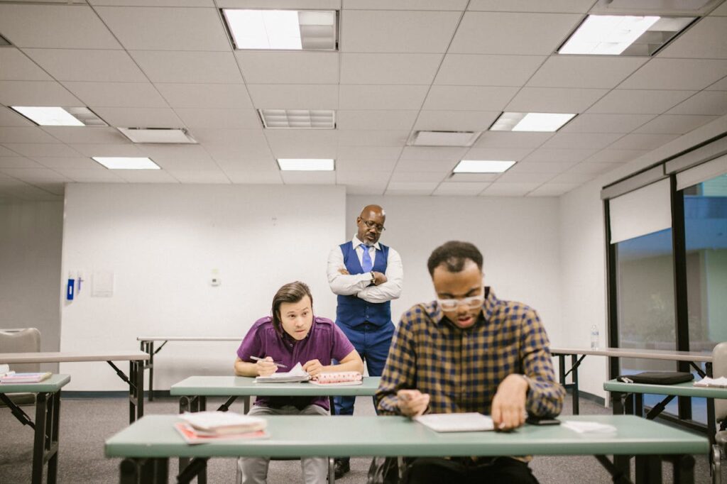 A teacher observes students taking a test in a brightly lit classroom environment.